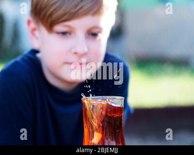 Kaukasischer Junge beobachtet einen Spritzer Tee in einer Tasse von einem fallenden Stück Zucker Stockfoto