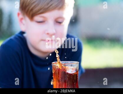 Kaukasischer Junge beobachtet einen Spritzer Tee in einer Tasse von einem fallenden Stück Zucker Stockfoto