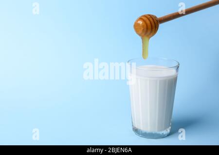 Weibliche Hände Gießen Honig zu Glas Milch auf blauem Hintergrund Stockfoto