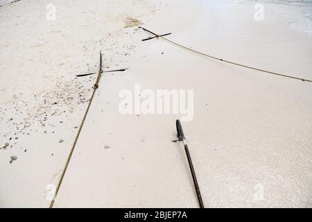 Drei Eisendelker sind am weißen Sand befestigt, der mit Seilen mit Fischerbooten am Wassertransportparkplatz am Strand der thailändischen Inselküste verbunden ist Stockfoto