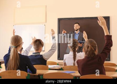 Schüler hören Lehrer und Heben Hände zu beantworten im Klassenzimmer Stockfoto