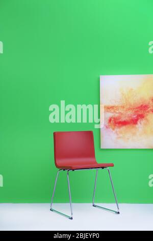 Moderner roter Stuhl in der Nähe der grünen Wand mit abstrakter Malerei Stockfoto