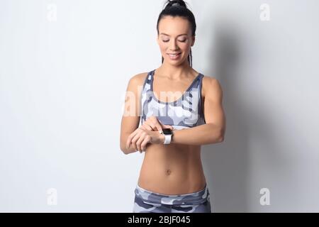 Sportliche junge Frau mit Fitness-Tracker auf hellem Hintergrund Stockfoto