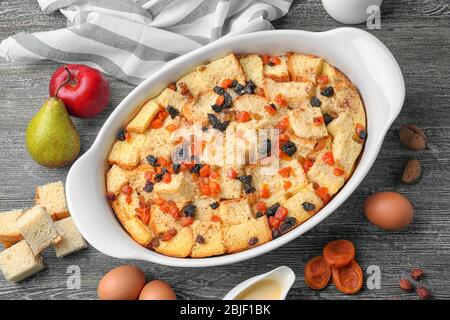 Frisch gebackener Brotpudding in Auflaufform und Zutaten auf Holztisch Stockfoto