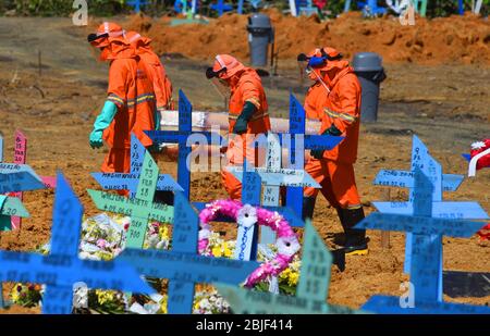 Manaus, Brasilien. April 2020. Friedhofspersonal in Schutzanzügen gegen die Ausbreitung von Covid-19 trägt einen Sarg zu einem Grab auf dem Friedhof. Angesichts der steigenden Zahl von Corona-Infektionen ist das Gesundheitssystem in Manaus an seiner Grenze. Vor einem Krankenhaus wurde ein gekühlter Behälter zur Aufbewahrung von Leichen aufgestellt, Massengräber wurden gegraben. Die Zahl der Covid-19-Todesfälle im Land stieg auf 5017 an - und übertraf China, das offiziell 4643 Todesfälle verzeichnete. Der ultrarechtsrechte Präsident Bolsonaro spielt das Virus ab. Kredit: Chico Batata/dpa/Alamy Live News Stockfoto