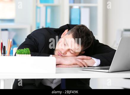 Junger Geschäftsmann schläft am Arbeitsplatz auf dem Tisch Stockfoto