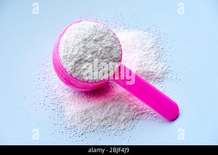 Weißes Waschpulver für die Waschmaschine auf pastellblauem Hintergrund und rosa Plastiklöffel für die Dosierung. Stockfoto