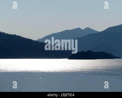 Blick vom Meer auf die bergigen Inseln, Küste am frühen Morgen. Malerische Seenlandschaft, Küste mit Hügeln von Wald in einem Nebel bedeckt Stockfoto