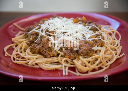 Nahaufnahme eines hausgemachten traditionellen Spaghetti Bolognese Gericht in einem roten Teller mit Parmesan Käse Stockfoto