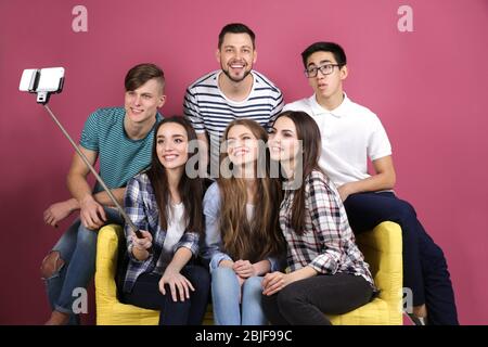 Junge Freunde, die Selfie machen, während sie auf dem Sofa vor farbigem Hintergrund sitzen Stockfoto