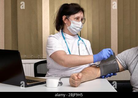 Der Therapeut misst den Blutdruck des Patienten und trifft Vorsichtsmaßnahmen im Zusammenhang mit der Pandemie der Coronavirus-Infektion Covid-19. Das hea Stockfoto