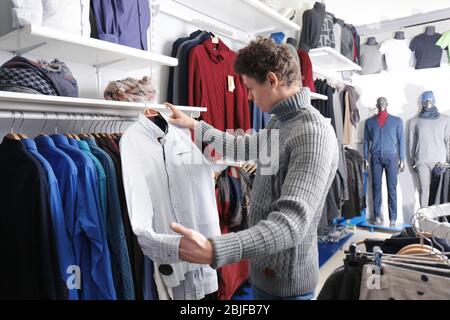 Schöner junger Mann, der Kleidung in einem modernen Geschäft auswählt Stockfoto
