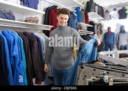 Schöner junger Mann, der Kleidung in einem modernen Geschäft auswählt Stockfoto