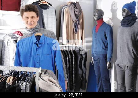 Schöner junger Mann, der Kleidung in einem modernen Geschäft auswählt Stockfoto