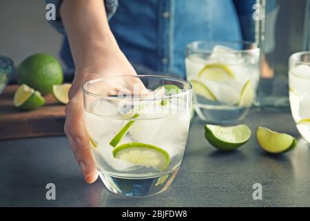 Weibliche Hand hält Alkohol Cocktail mit Limette auf dem Tisch Stockfoto