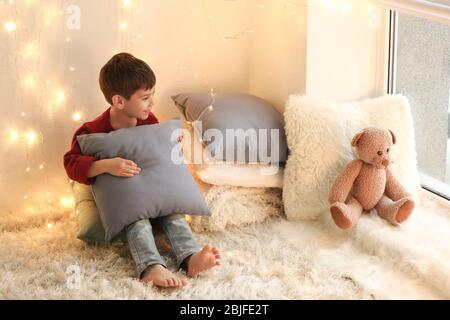 Niedlicher kleiner Junge mit Kissen sitzt auf dem Boden zu Hause Stockfoto