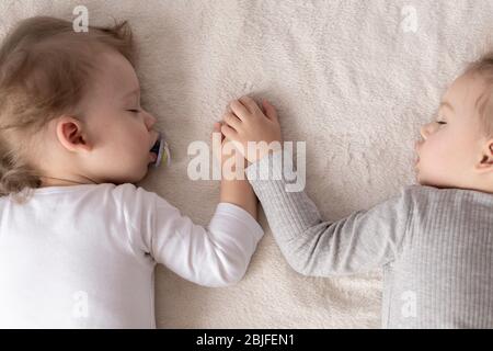 Kindheit, Schlaf, Entspannung, Familie, Lifestyle-Konzept - zwei kleine Kinder im Alter von 2 und 3 Jahren in weiß-beigem Body schlafen auf einem beige Stockfoto