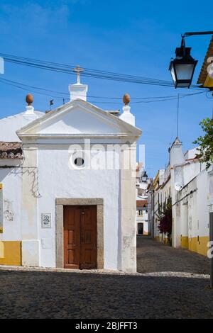 Typische Straßenszene aus weißen und gelben Häusern, Laternen und engen Kopfsteinpflasterstraßen in Evora, Portugal Stockfoto