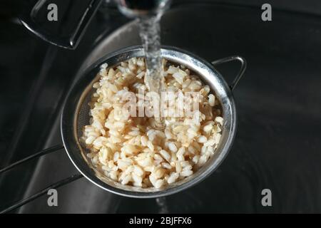 Brauner Reis mit Wasser im Sieb waschen Stockfoto