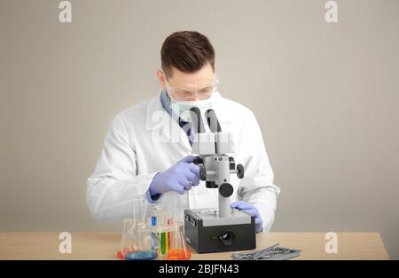 Junger Arzt arbeitet mit Mikroskop am Tisch auf hellem Hintergrund Stockfoto