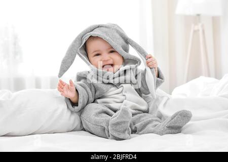 Niedliches kleines Baby im Hasenkostüm, das zu Hause auf dem Bett sitzt Stockfoto