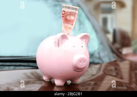 Keramik Sparschwein mit Banknote auf Haube des Autos Stockfoto