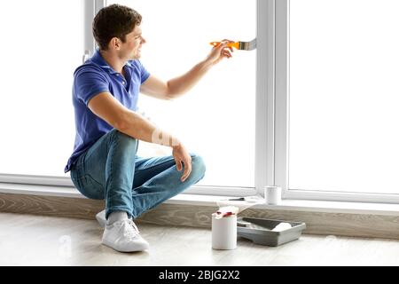 Junger Mann, der Fenster zu Hause malt Stockfoto