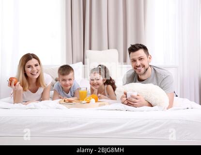 Glückliche lächelnde Familie, die im Bett gefrühstückt hat Stockfoto