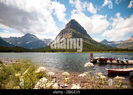 Mountain Peak Landschaft Szene von Grinnell Point und Swiftcurrent Lake im Glacier Nationalpark. Boote dockten im Wasser mit einem lebendigen blauen Himmel abov Stockfoto