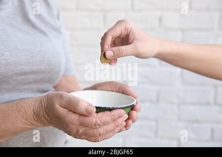 Weibliche Hand, die Münze in die Schüssel in die Hände der älteren Frau, Nahaufnahme. Armutskonzept Stockfoto