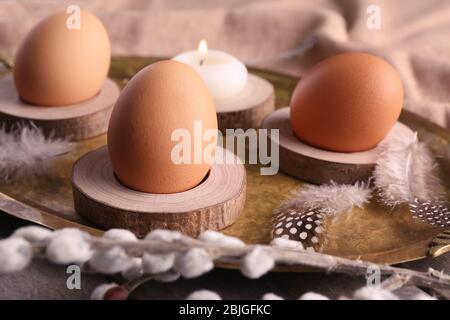 Holzständer mit Ostereiern und Kerze auf goldenem Tablett Stockfoto