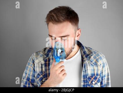 Junger Mann, der Vernebler für Asthma und Atemwegserkrankungen auf hellem Hintergrund verwendet Stockfoto