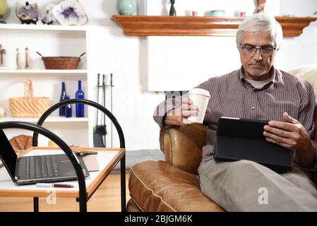 Nahaufnahme eines Mannes, der während der Sperrung von Covid-19 von zu Hause aus arbeitet. Eine Kaffeepause mit seinem Tablet-Computer machen. Stockfoto