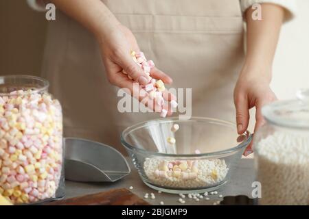 Frau hinzufügen Marshmallow in Glasschüssel mit knusprigen Reisbällchen auf dem Tisch Stockfoto