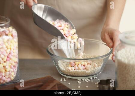 Frau hinzufügen Marshmallow in Glasschüssel mit knusprigen Reisbällchen auf dem Tisch Stockfoto