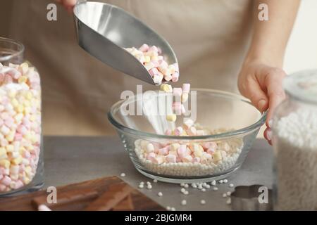 Frau hinzufügen Marshmallow in Glasschüssel mit knusprigen Reisbällchen auf dem Tisch Stockfoto