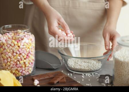 Frau hinzufügen Marshmallow in Glasschüssel mit knusprigen Reisbällchen auf dem Tisch Stockfoto