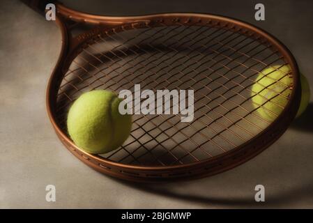 Nahaufnahme eines Tennisschlägers und zwei Bälle auf einer Hartplatz-Oberfläche mit starkem Seitenlicht. Stockfoto
