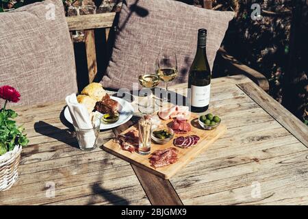 Charcuterie-Board mit Weißwein im Freien serviert. Eine Platte mit Schinken und Speck Scheiben mit Gurken auf einem Holzbrett Stockfoto