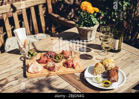 Charcuterie-Board mit Weißwein im Freien serviert. Eine Platte mit Schinken und Speck Scheiben mit Gurken auf einem Holzbrett Stockfoto