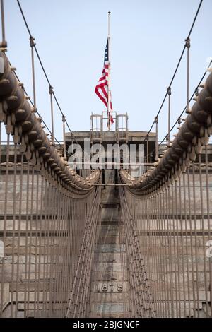 Detail von Drähten und Turm mit amerikanischer Flagge auf der historischen Brooklyn Bridge Stockfoto