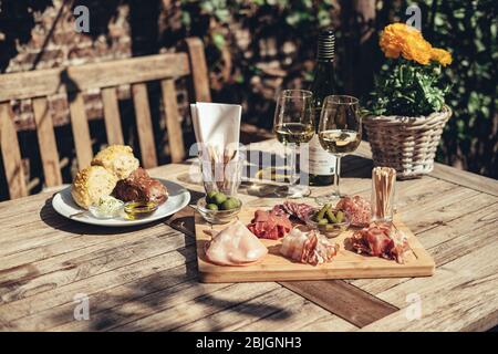 Charcuterie-Board mit Weißwein im Freien serviert. Eine Platte mit Schinken und Speck Scheiben mit Gurken auf einem Holzbrett Stockfoto