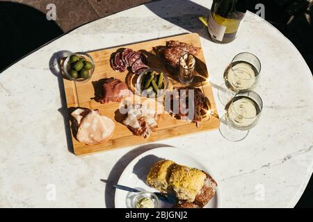 Charcuterie-Board mit Weißwein im Freien serviert. Eine Platte mit Schinken und Speck Scheiben mit Gurken auf einem Holzbrett. Draufsicht Stockfoto