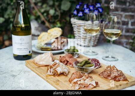 Zwei Gläser und eine Flasche Weißwein mit Gourmet-Tafel auf einem runden Marmortisch. Gartenparty. Stockfoto