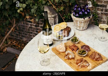 Zwei Gläser und eine Flasche Weißwein mit Gourmet-Tafel auf einem runden Marmortisch. Gartenparty. Stockfoto