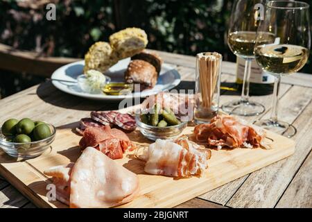 Zwei Gläser und eine Flasche Weißwein mit Gourmet-Tafel auf einem runden Marmortisch. Gartenparty. Stockfoto