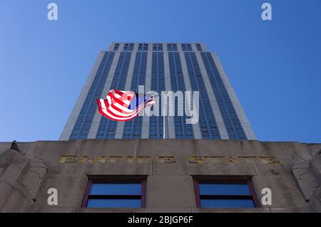 Blick direkt auf das historische Empire State Building mit winkender amerikanischer Flagge in New York City Stockfoto