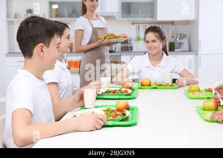 Kinder sitzen am Tisch in der Schulkantine während des Mittagessens Stockfoto