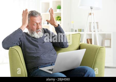 Schöner älterer Mann sitzt im Sessel mit Laptop Stockfoto