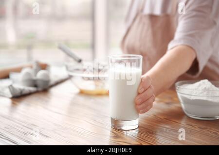 Alte Frau hält Glas mit frischer Milch auf dem Tisch Stockfoto